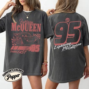 May include: Dark gray t-shirt featuring Lightning McQueen from the Cars movie. The front graphic includes the character's image, the text "Lightning McQueen," and "95." The back displays a large "95" and "Lightning McQueen" in white.