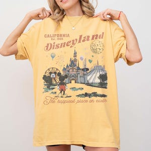 May include: Yellow t-shirt with a Disneyland graphic. The design includes the Disneyland logo, a castle, Mickey Mouse, and the text "The happiest place on earth". The shirt is a vintage style.