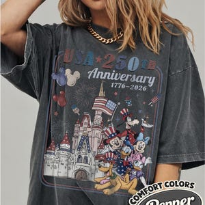Puede incluir: Camiseta gris oscuro con un dise&ntilde;o que conmemora el 250 aniversario de EE. UU., con personajes de Disney y un castillo. El dise&ntilde;o incluye el texto "USA 250th Anniversary 1776-2026" y el logotipo Comfort Colors Pepper.