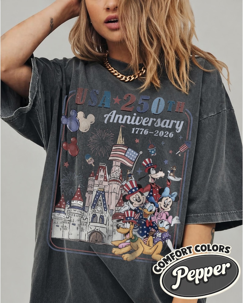 Puede incluir: Camiseta gris oscuro con un dise&ntilde;o que conmemora el 250 aniversario de EE. UU., con personajes de Disney y un castillo. El dise&ntilde;o incluye el texto "USA 250th Anniversary 1776-2026" y el logotipo Comfort Colors Pepper.