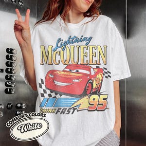 K&ouml;nnte beinhalten: Wei&szlig;es T-Shirt mit einem Aufdruck von Lightning McQueen aus dem Film Cars. Das Design enth&auml;lt den Text "Lightning McQueen", "Think Fast" und die Nummer "95". Das Shirt ist mit "Comfort Colors" gekennzeichnet.