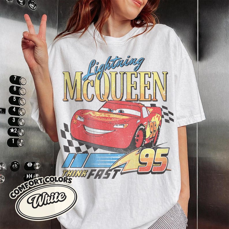 K&ouml;nnte beinhalten: Wei&szlig;es T-Shirt mit einem Aufdruck von Lightning McQueen aus dem Film Cars. Das Design enth&auml;lt den Text "Lightning McQueen", "Think Fast" und die Nummer "95". Das Shirt ist mit "Comfort Colors" gekennzeichnet.