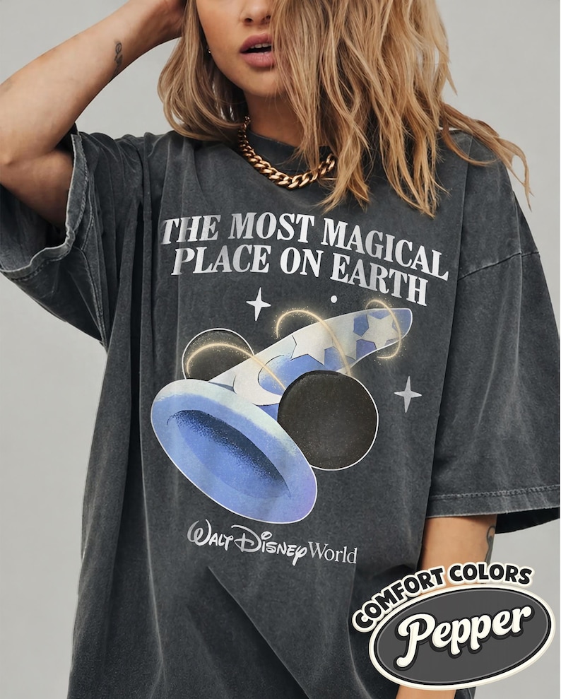 K&ouml;nnte beinhalten: Dunkelgraues T-Shirt mit dem Text "THE MOST MAGICAL PLACE ON EARTH" und einer Grafik eines blauen Hutes mit Sternen. Das Shirt zeigt auch das Walt Disney World-Logo und die Worte "COMFORT COLORS Pepper".