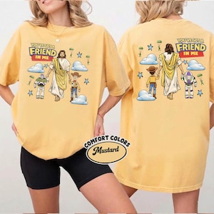 May include: Mustard-coloured t-shirt with the text "YOU'VE GOT A FRIEND IN ME" above a graphic of Jesus, Woody, and Buzz Lightyear. The back of the shirt has the same design. The shirt is from Comfort Colors.