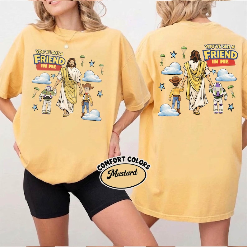 May include: Mustard-coloured t-shirt with the text "YOU'VE GOT A FRIEND IN ME" above a graphic of Jesus, Woody, and Buzz Lightyear. The back of the shirt has the same design. The shirt is from Comfort Colors.