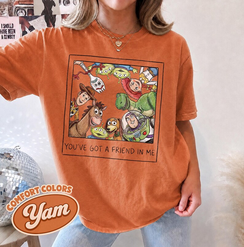 Puede incluir: Camiseta naranja Comfort Colors con un gr&aacute;fico enmarcado de personajes de Toy Story. La frase "YOU'VE GOT A FRIEND IN ME" est&aacute; impresa debajo del gr&aacute;fico. La camiseta tambi&eacute;n tiene los logotipos de Comfort Colors y Yam.