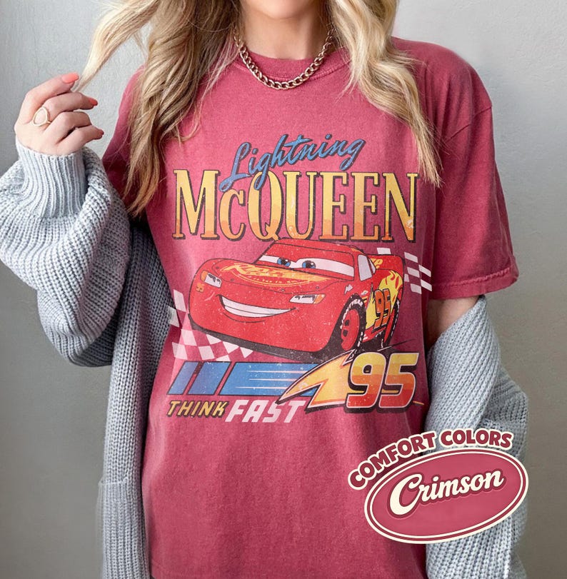 K&ouml;nnte beinhalten: Karmesinrotes T-Shirt mit Lightning McQueen aus dem Film Cars. Das Design zeigt das Bild der Figur, den Text "Lightning McQueen" und "Think Fast 95". Das Shirt hat einen Vintage-Look mit einem Comfort Colors-Label.