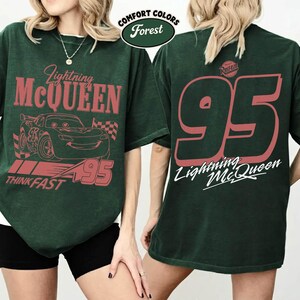 May include: Forest green t-shirt featuring Lightning McQueen graphics. The front displays the car, the text "Lightning McQueen", "95", and "Think Fast". The back has a large "95" and "Lightning McQueen" text.