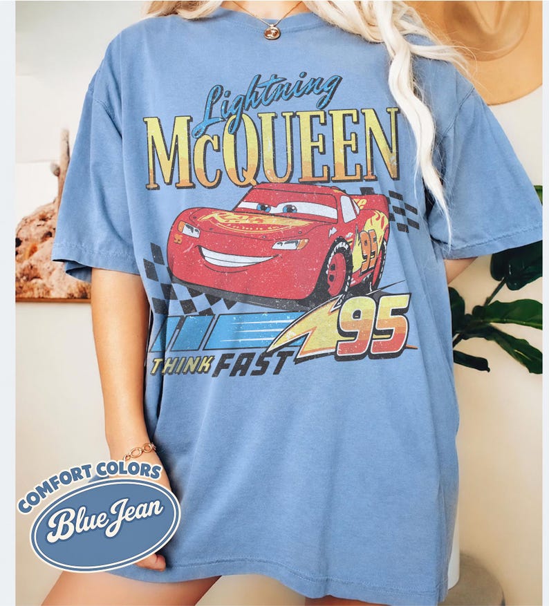 K&ouml;nnte beinhalten: Blaues T-Shirt mit kurzen &Auml;rmeln mit Lightning McQueen aus dem Film Cars. Die Grafik enth&auml;lt den Text "Lightning McQueen" &uuml;ber einem roten Rennwagen mit der Nummer 95. Der Satz "Think Fast" steht darunter.