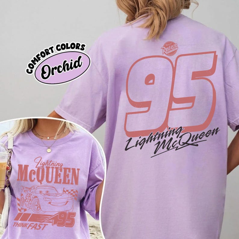 May include: A light purple t-shirt featuring the text "Lightning McQueen" and the number "95" in coral. The shirt also has the words "Think Fast" and the phrase "Comfort Colors Orchid".