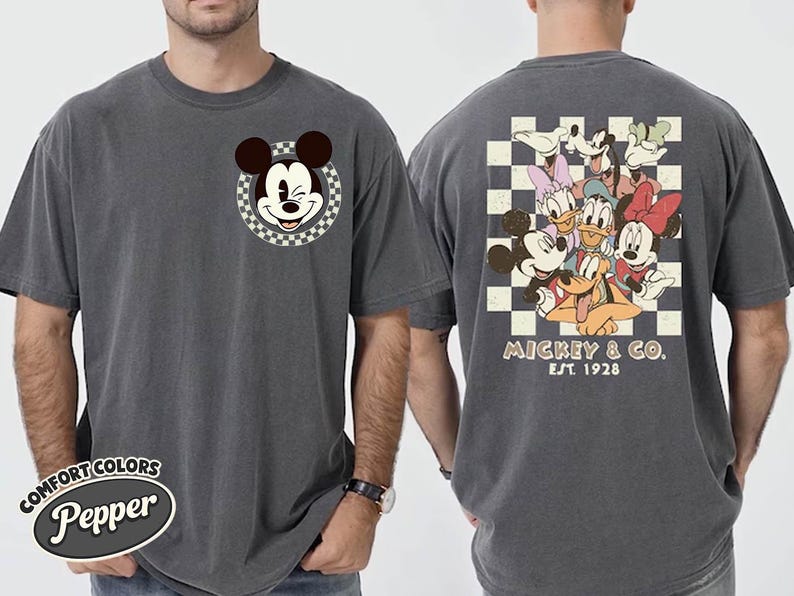 May include: Dark grey t-shirt featuring Mickey Mouse winking in a checkered circle on the front. The back displays a group of Disney characters on a checkered background, with "Mickey & Co. Est. 1928" printed below. The shirt is labeled "Comfort Colors Pepper".
