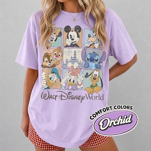 May include: A lilac-colored t-shirt featuring a grid of Disney characters including Mickey Mouse, Minnie Mouse, Donald Duck, and Stitch. The words "Walt Disney World" are printed below the grid. The shirt also has the words "Comfort Colors" and "Orchid" printed on it.