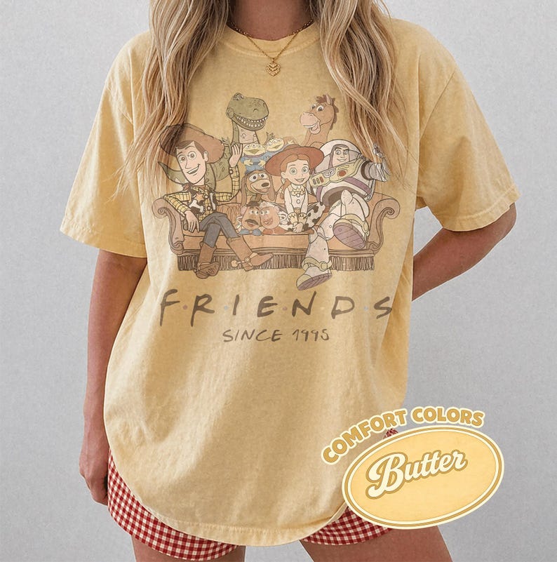 Puede incluir: Camiseta amarilla clara con un dise&ntilde;o de los personajes de Toy Story en un dise&ntilde;o tem&aacute;tico de Friends. La camiseta tiene el texto "FRIENDS SINCE 1995" y una etiqueta "Comfort Colors Butter".