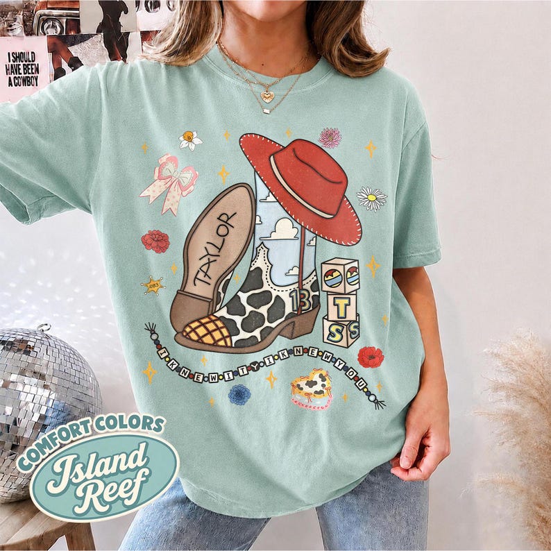 Peut inclure: Un t-shirt vert clair avec une impression graphique repr&eacute;sentant une botte de cow-boy &agrave; motifs de vache, un chapeau de cow-boy rouge et des blocs avec le texte 13 et TS. Le motif inclut un ruban, des fleurs et le texte I KNEW IT I KNEW YOU.