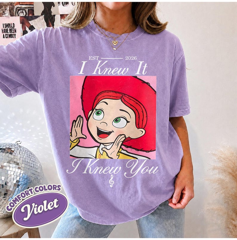 May include: A violet short-sleeved t-shirt featuring a graphic of a cartoon character with red hair and a red hat. The text reads EST 2026 I Knew It I Knew You. The shirt has a crew neckline and a relaxed fit, showcasing a vintage-inspired design.