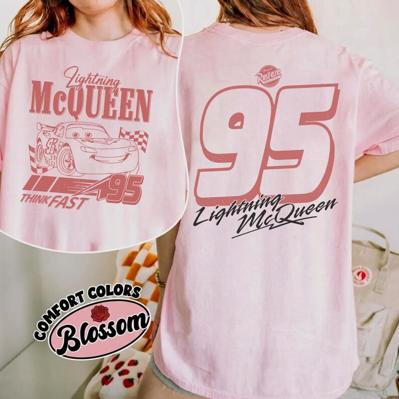 May include: Light pink t-shirt featuring Lightning McQueen graphics. The front displays the character with text reading "Lightning McQueen," "95," and "Think Fast." The back features a large "95" and "Lightning McQueen" in a script font. The shirt has a "Comfort Colors Blossom" logo.