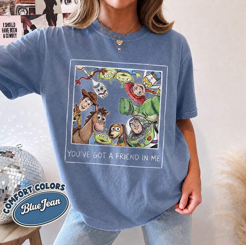 Puede incluir: Camiseta azul vaquero con una ilustraci&oacute;n enmarcada de personajes de la pel&iacute;cula de animaci&oacute;n Toy Story. La frase "YOU'VE GOT A FRIEND IN ME" est&aacute; impresa debajo de la ilustraci&oacute;n. La camiseta tambi&eacute;n tiene las palabras "COMFORT COLORS" y "Blue Jean".