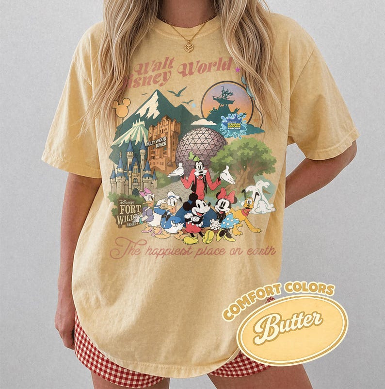 Pu&ograve; includere: T-shirt giallo senape con grafica Disney. Il design include Topolino, Minnie, Paperino e Pippo, con la scritta "Walt Disney World" e "The happiest place on earth".