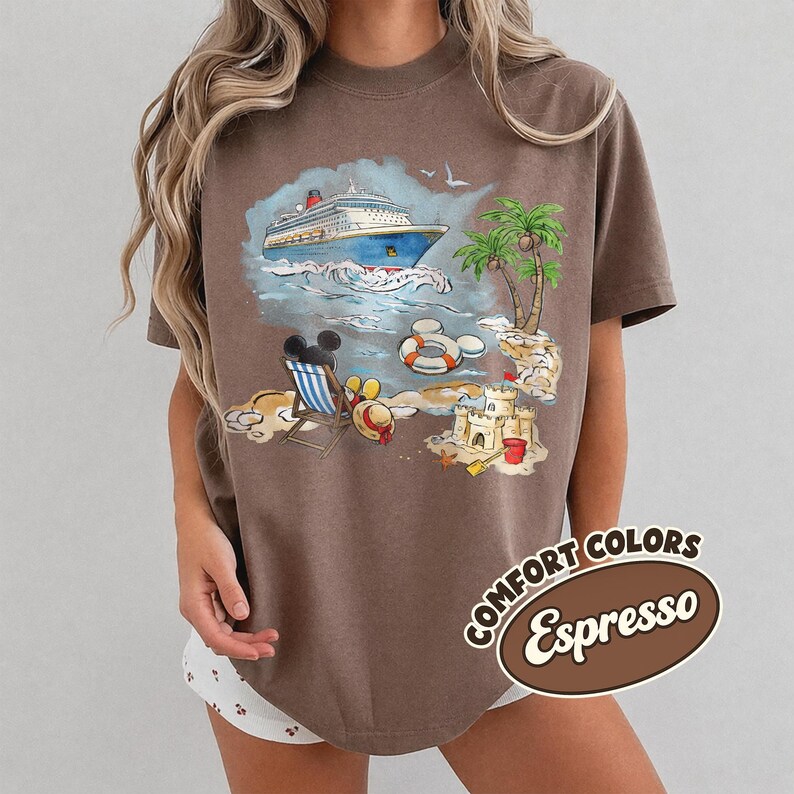 Op de afbeelding: Bruin T-shirt met een strandthema. Het ontwerp bevat een cruiseschip, palmbomen en een zandkasteel. Een strandstoel, Mickey Mouse oren en een reddingsboei zijn ook zichtbaar. De tekst "COMFORT COLORS Espresso" staat rechtsonder.