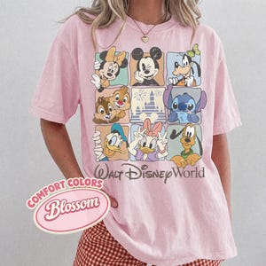 May include: Pink t-shirt featuring a grid of Disney characters including Mickey Mouse, Minnie Mouse, Goofy, Chip and Dale, Stitch, Donald Duck, Daisy Duck, and Pluto. The shirt also has the text "Walt Disney World".