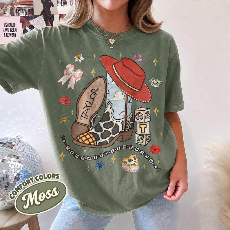 Peut inclure: Un t-shirt vert mousse avec une impression graphique d'une botte de cow-boy &agrave; motifs de vache, un chapeau rouge, le nom TAYLOR, le chiffre 13, des blocs empil&eacute;s avec les lettres T, S et un collier de perles avec le texte I KNEW IT I KNEW YOU.