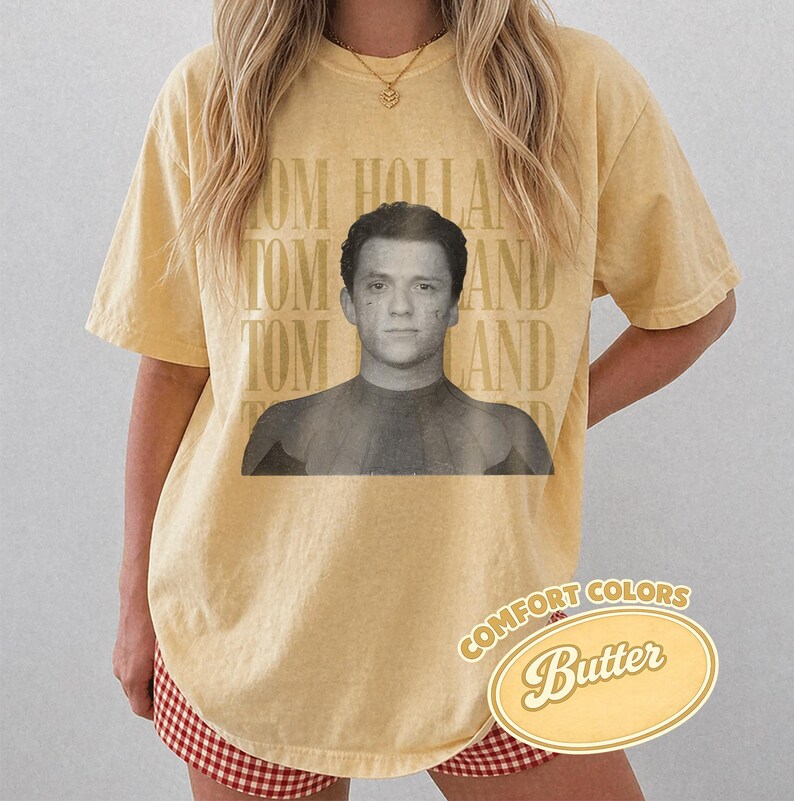 Peut inclure: T-shirt jaune beurre avec une image en noir et blanc de Tom Holland. Les mots "TOM HOLLAND" sont imprim&eacute;s verticalement sur le c&ocirc;t&eacute; gauche. Les mots "COMFORT COLORS" et "Butter" sont imprim&eacute;s sur un ovale jaune.