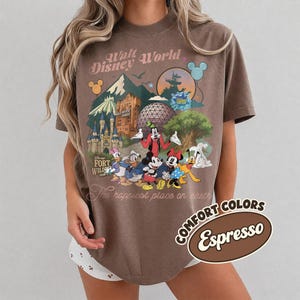 Pu&ograve; includere: T-shirt color espresso con grafica vintage di Walt Disney World. Il design include monumenti iconici del parco, personaggi dei cartoni animati e la frase "The happiest place on earth."