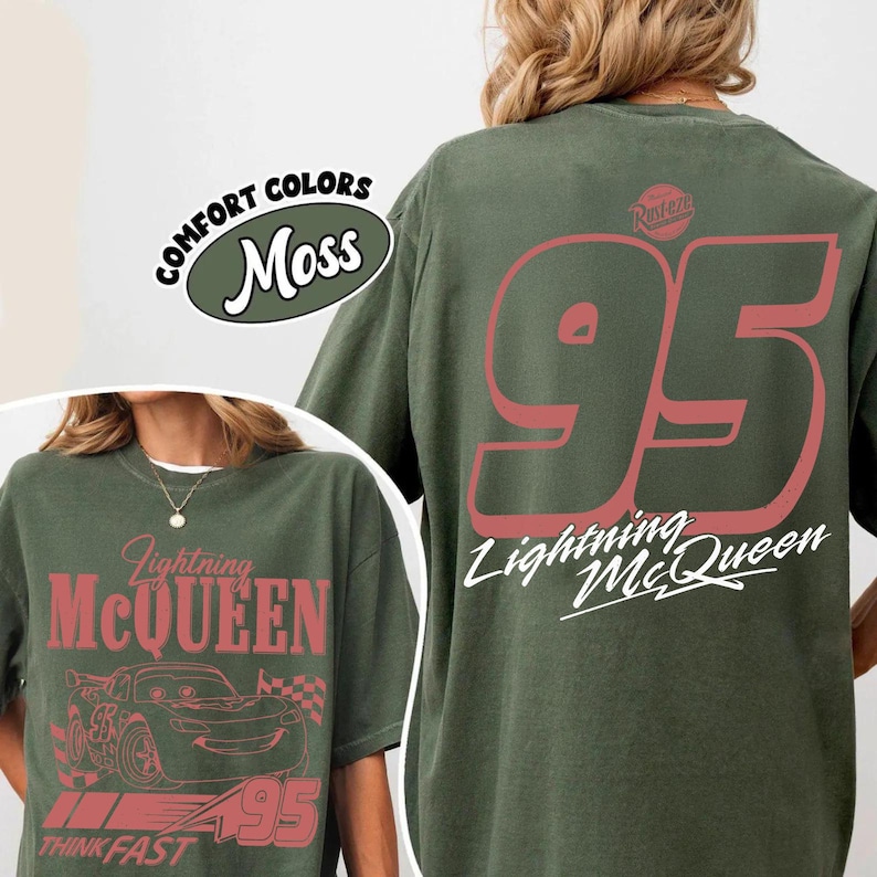 May include: Moss green t-shirts featuring Lightning McQueen graphics. One shirt displays "Lightning McQueen" and a car graphic, the other shows the number "95" and "Lightning McQueen" text. The shirts have a vintage look.
