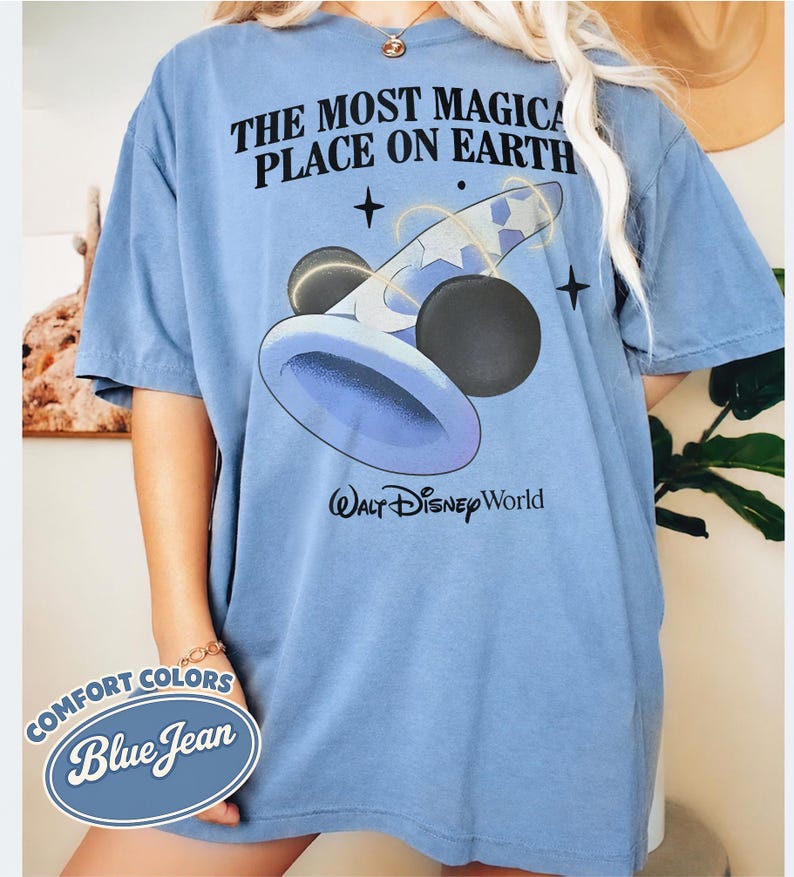 K&ouml;nnte beinhalten: Blaues Jeans-T-Shirt mit dem Text "THE MOST MAGICAL PLACE ON EARTH" und einer Grafik eines Zauberhuts und Mickey-Mouse-&auml;hnlichen Kugeln. Die Worte "Walt Disney World" sind darunter gedruckt. Das Shirt hat auch ein "Comfort Colors Blue Jean"-Etikett.
