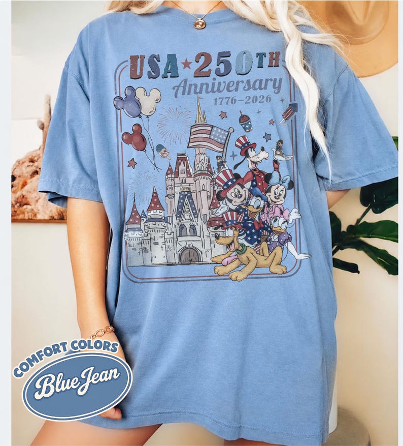 Puede incluir: Camiseta azul claro con un dise&ntilde;o gr&aacute;fico que celebra el 250 aniversario de EE. UU., con personajes de Disney, un castillo y fuegos artificiales. El dise&ntilde;o incluye el texto "USA 250th Anniversary 1776-2026" y las palabras "Comfort Colors Blue Jean".