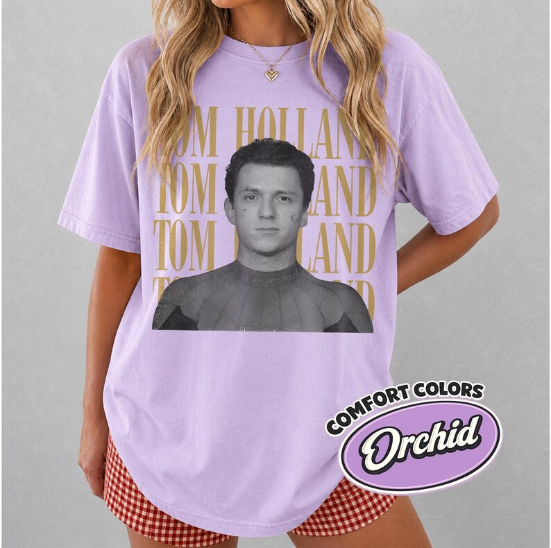 Peut inclure: T-shirt lilas avec une image en noir et blanc de Tom Holland en Spider-Man. Les mots "TOM HOLLAND" sont imprim&eacute;s en or. Le t-shirt porte &eacute;galement une &eacute;tiquette Comfort Colors Orchid.