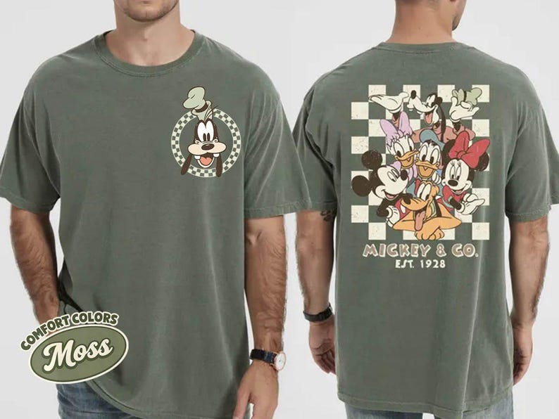 May include: Moss green t-shirt featuring a cartoon image of Goofy on the front and a group of Disney characters on the back. The back design includes Mickey Mouse, Minnie Mouse, Donald Duck, Daisy Duck, and Goofy. The text "Mickey & Co. EST 1928" is also on the back.