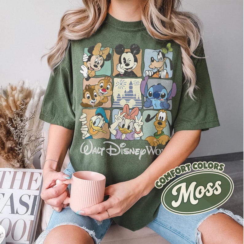 May include: Green t-shirt featuring a grid of Disney characters including Mickey Mouse, Minnie Mouse, Donald Duck, and Stitch. The shirt has the words "Walt Disney World" printed on it. The shirt is a moss green color.