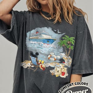 Op de afbeelding: Donkergrijze t-shirt met een kleurrijke strandsc&egrave;ne: cruiseschip, palmbomen, zandkasteel. De afbeelding bevat Mickey Mouse en de tekst "Comfort Colors Pepper".