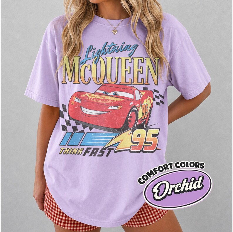 K&ouml;nnte beinhalten: Ein lila T-Shirt mit einer Grafik von Lightning McQueen aus dem Film Cars. Das Design enth&auml;lt den Text "Lightning McQueen", "95" und "Think Fast". Das Shirt hat auch ein "Comfort Colors"-Label.