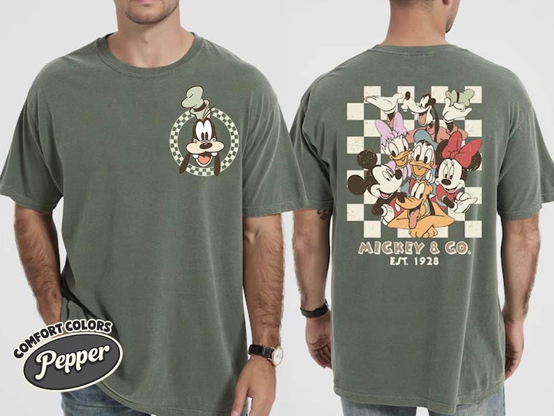 May include: Olive green t-shirt featuring Goofy on the front and a group of Disney characters on the back. The back design includes Mickey Mouse, Minnie Mouse, Donald Duck, Daisy Duck, Pluto, and Goofy. The text "Mickey & Co. EST. 1928" is also visible.