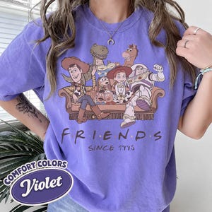 Puede incluir: Camiseta violeta Comfort Colors con un gr&aacute;fico de personajes de Toy Story en un sof&aacute; marr&oacute;n, con la palabra "FRIENDS" y "SINCE 1995" en texto negro. La camiseta tambi&eacute;n tiene un logotipo "Violet".