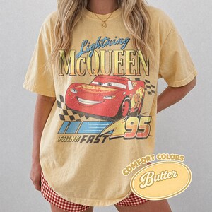 K&ouml;nnte beinhalten: Gelbes T-Shirt mit Lightning McQueen aus dem Film Cars. Die Grafik enth&auml;lt den Text "Lightning McQueen", "95" und "Think Fast". Das Shirt ist mit "Comfort Colors Butter" gekennzeichnet.