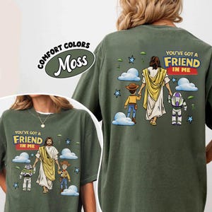 May include: Moss green t-shirt featuring the text "YOU'VE GOT A FRIEND IN ME" and a graphic of Jesus, a cowboy, and a space ranger. The shirt also has the words "COMFORT COLORS" and "Moss" in a circle.