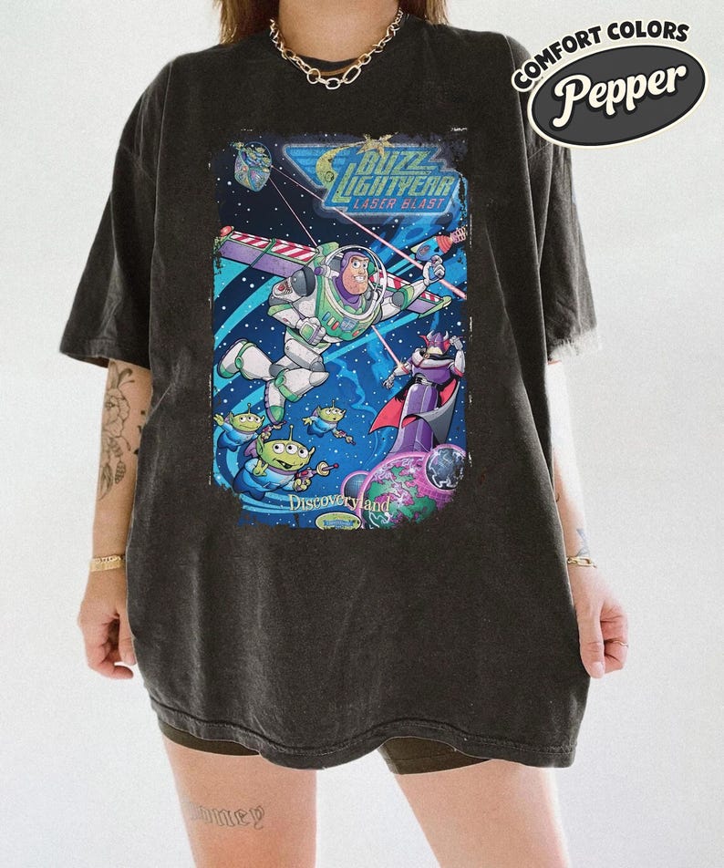 Pode incluir: Uma t-shirt preto carv&atilde;o com uma estampa gr&aacute;fica de Buzz Lightyear, Zurg e alien&iacute;genas verdes no espa&ccedil;o. O texto diz Buzz Lightyear Laser Blast e Disneyland. Um log&oacute;tipo Comfort Colors Pepper &eacute; vis&iacute;vel no canto superior direito.