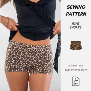 Könnte beinhalten: Eine weiße Keramik-Tasse mit schwarzem Henkel und dem Text "But First, Coffee" in schwarzer, handschriftlicher Schrift. Die Tasse steht auf einer weißen Oberfläche.