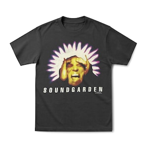 May include: Black t-shirt featuring the band name "SOUNDGARDEN" in white block letters. The graphic is a distressed image of a person with their hands on their head, surrounded by a white and purple burst.