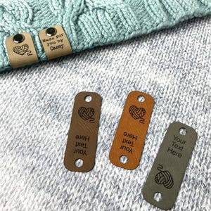 May include: Leather tags with a yarn ball and heart design, and the text "Your Text Here". The tags are in shades of brown and grey, with a light blue knitted item in the background. One tag says "Made for you by Casey".
