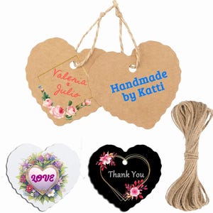 Pode incluir: Etiquetas artesanais em forma de coração com bordas onduladas, algumas com desenhos florais e texto. Uma etiqueta diz "Handmade by Katti" em azul. Um rolo de barbante também está presente. Medidas em centímetros.