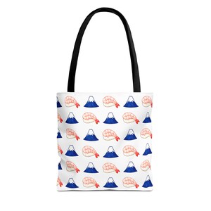 May include: A white tote bag with black handles featuring a repeating pattern of pink shrimp sushi nigiri and blue mountain peaks with white snow-capped tops. The design is arranged in a grid layout across the front of the fabric bag.