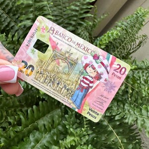 Może przedstawiać: Banknot dwudziestu pesos z Banco de M&eacute;xico z postacią z kresk&oacute;wki w kapeluszu truskawkowym. Banknot ma r&oacute;żowo-białą kolorystykę z napisem "Veinte Pesos".