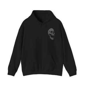 May include: Black hoodie with a front pocket and drawstring. A detailed, textured skull graphic is printed on the upper left chest. The hoodie is made of a soft material.