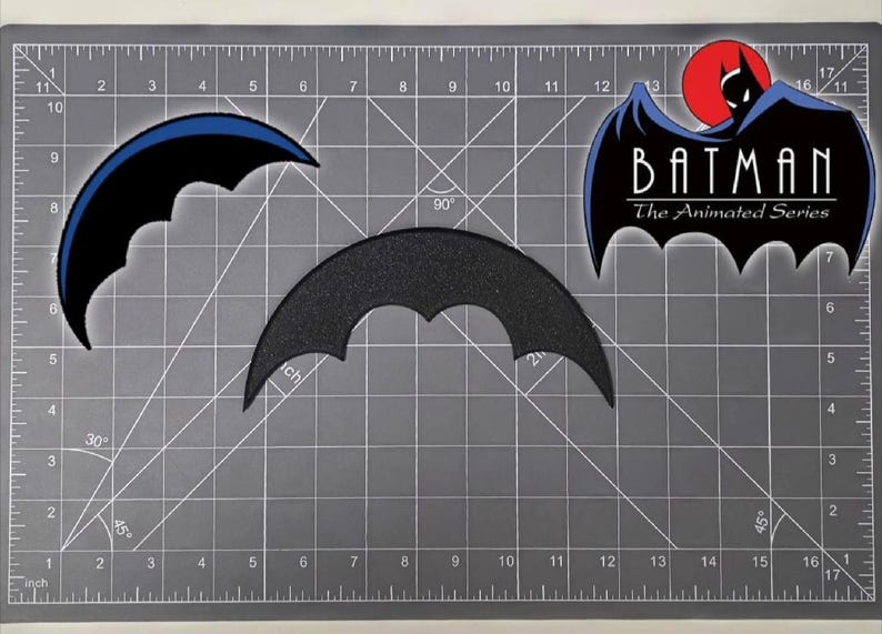 May include: Three Batman-themed patches on a gray cutting mat. One patch is a black bat symbol with a blue outline, another is a textured black bat symbol, and the third features the Batman logo from "The Animated Series."