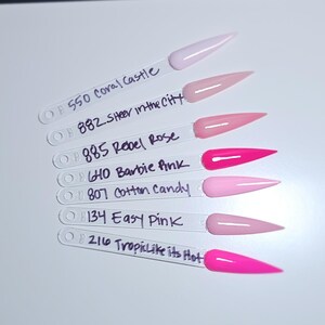 May include: Seven clear plastic nail polish display sticks with pointed tips, each featuring a different shade of pink polish. The sticks are labeled with numbers and names: 550 Coral Castle, 882 Sheer in the City, 885 Rebel Rose, 640 Barbie Pink, 807 Cotton Candy, 134 Easy Pink, and 216 Tropic Like its Hot.