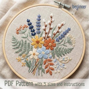 May include: A floral embroidery design in a wooden hoop. The design features a bouquet of colorful flowers, including blue, orange, yellow, and white blooms, with green foliage. The text "beginner" is in the upper right corner. The text "PDF Pattern with 5 sizes and instructions" is at the bottom.